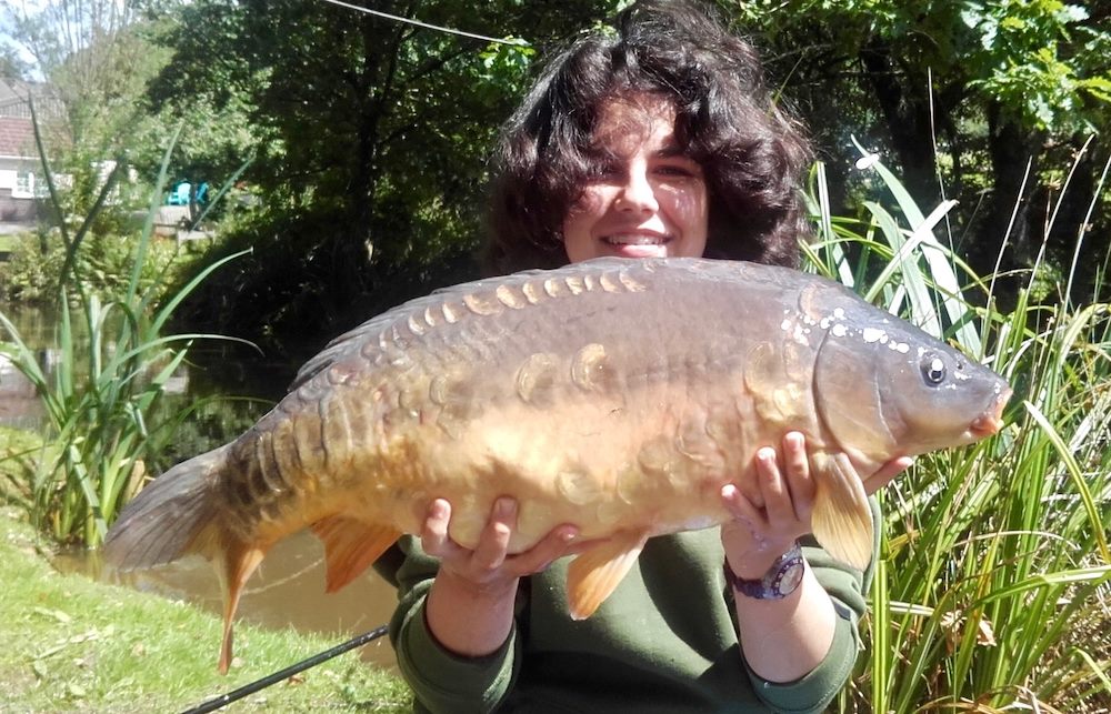 young woman beams while holding a large common carp she has caught at a South Farm Holiday Cottages & Fishery