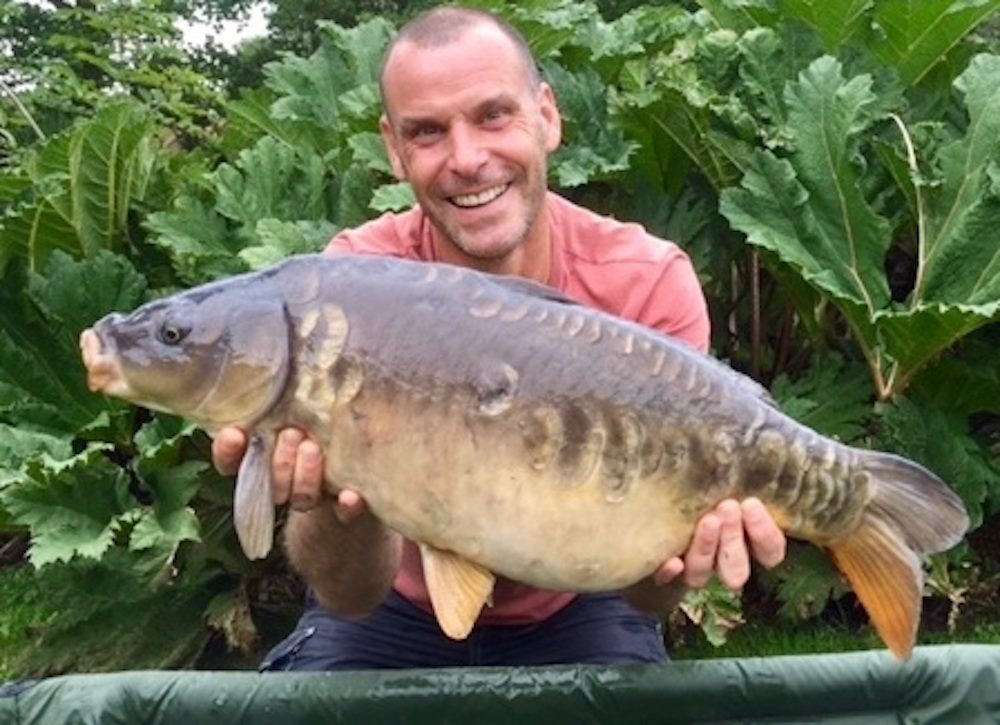 angler beams while holding a large specimen of mirror carp, known for its unique scale pattern.