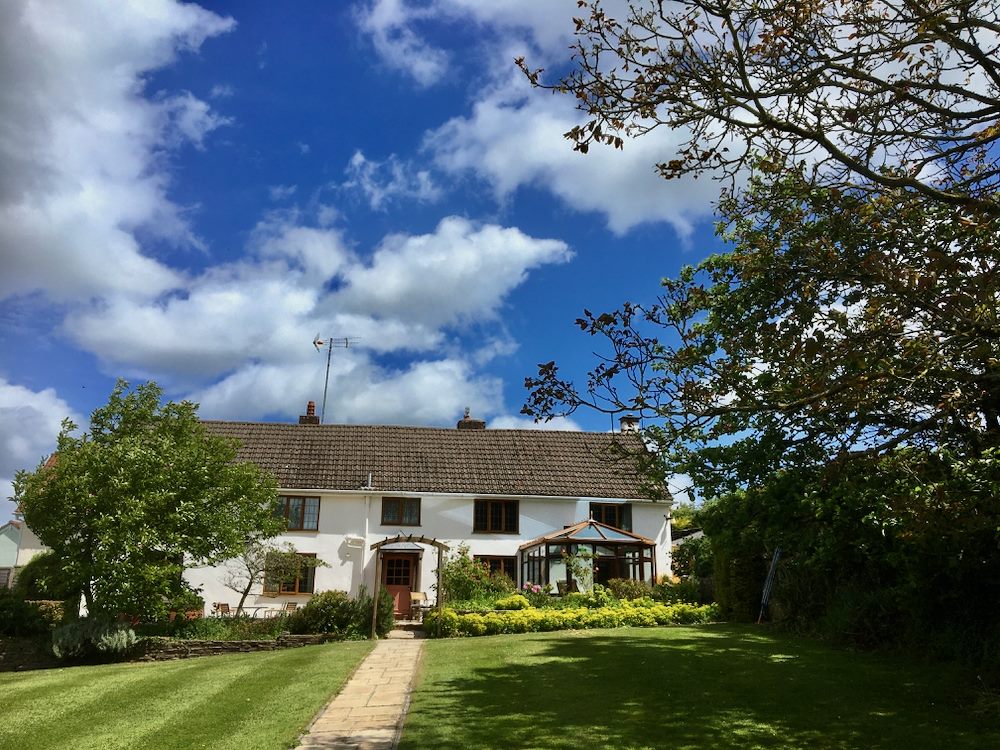 A picturesque view of the farm house of the South Farm Holiday Cottages & Fishery in the UK. The white cottage features a conservatory and is surrounded by a well-maintained garden with a stone path.
