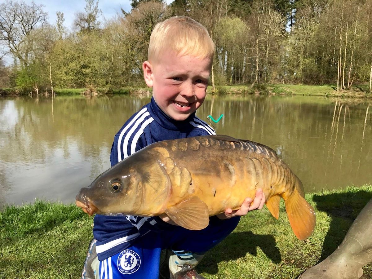 A happy young angler in the UK displays a sizable common carp he has just caught.