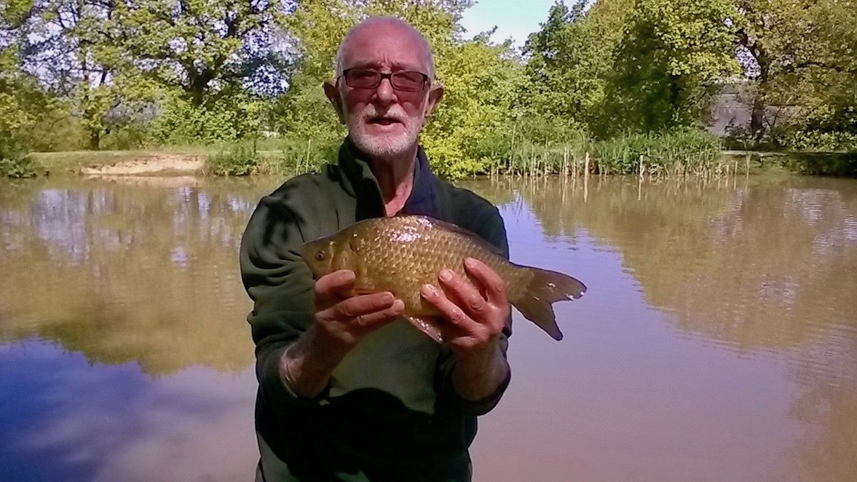 proud angler displays a small, golden carp, he has caught at Lower Ram lake.