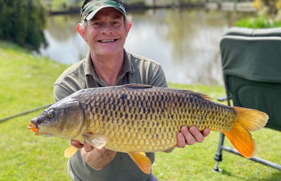 A successful carp fishing moment in the UK. An angler beams while holding a large common carp, showcasing the rewards of fishing at a South Farm Holiday Cottages & fishery.