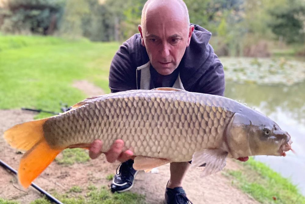A successful fishing moment at South Farm Holiday Cottages & Fishery in Devon. A man holds up a large carp he has caught.