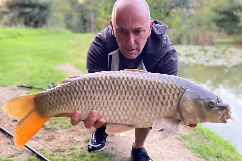 A successful fishing moment at South Farm Holiday Cottages & Fishery in Devon. A man holds up a large carp he has caught.